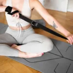 a woman sitting on a mat holding a strap