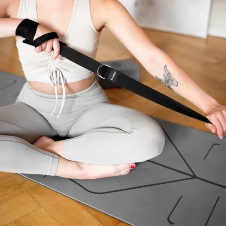 a woman sitting on a mat holding a strap