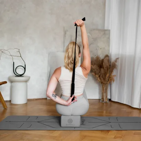 a woman sitting on a yoga mat holding a strap