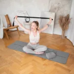 a woman sitting on a yoga mat holding a strap over her head