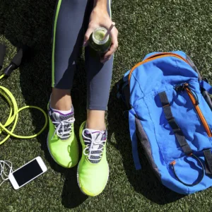 Sporty woman holding green juice sitting on grass