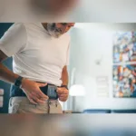 Mees kinnitab Compex ComfortTENS Back vööle magnetitega juhtploki ja valib programmi
