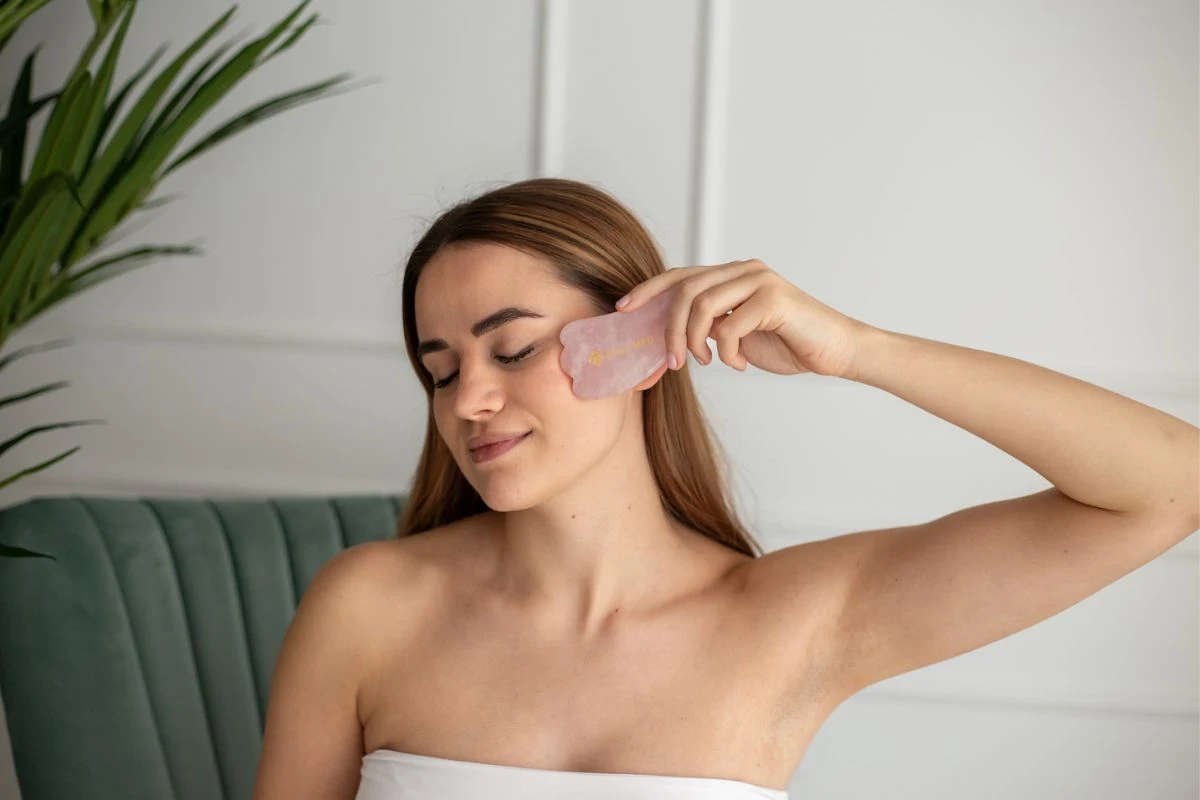 Naine masseerib roosa Gua Sha plaadiga põsesarna piirkonda